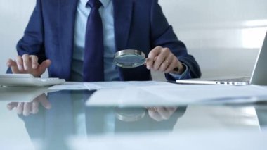 İş adamı, mali verileri büyüteç ve hesap makinesiyle analiz ediyor, denetleme veya teftiş yapıyor. İş dünyasında denetim ve vergi teması.
