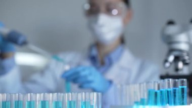 Laboratuvar tüpleri odaklandı, yakın görüş. Kadın araştırmacı, arka planda bir mikro pipet kullanıyor. Tıp ve Bilim.