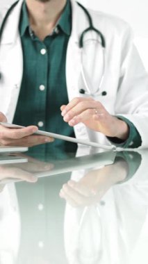 Modern sağlık ortamında dijital tablet kullanan yeşil gömlekli bir doktor hasta verileriyle etkileşime geçiyor. Tıp konsepti.