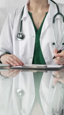 Kadın doktor, pano kullanıyor ve tıbbi bir ofisteki cam masaya notlar alıyor, dikey açıdan yakından bakıyor. Tıp konsepti.