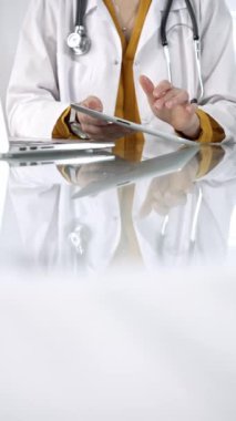 Stetoskop takan, laboratuvar önlüğünün altında sarı bluz giyen kimliği belirsiz doktor kadın, modern sağlık ortamında dijital tablet kullanıyor, hasta verileriyle etkileşimde, dikey portre ile. Tıp konsepti.