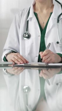 Kadın doktor, pano kullanıyor ve tıbbi bir ofisteki cam masaya notlar alıyor, dikey açıdan yakından bakıyor. Tıp konsepti.