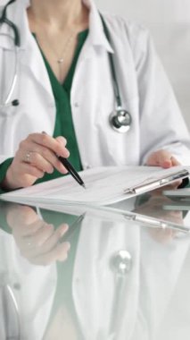 Hastane ortamındaki kadın doktor tıbbi raporlara işaret ediyor, yakın çekim çekimde uzmanlık gösteriyor. İlaç.