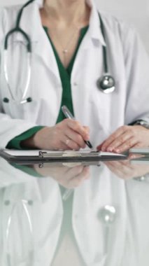Kadın doktor, pano kullanıyor ve tıbbi bir ofisteki cam masaya notlar alıyor, dikey açıdan yakından bakıyor. Tıp konsepti.
