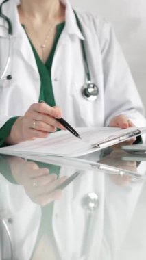 Hastane ortamındaki kadın doktor tıbbi raporlara işaret ediyor, yakın çekim çekimde uzmanlık gösteriyor. İlaç.