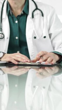 Steteskop ve laboratuvar önlüğü giyen erkek doktor, masadaki bir hastaya dizüstü bilgisayarla teşhis koymayı açıklarken elleriyle işaret ediyor. İlaç..