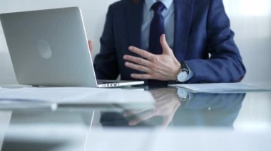 Mavi takım elbiseli bir işadamı, elleri cam ekrandaki dizüstü bilgisayarın yanında otururken parlak bir ofiste, internet iletişiminde, yakın çekim görüntüsünde oturuyor. İş konsepti.