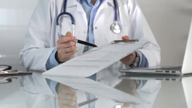 Hastane ortamındaki kadın doktor tıbbi raporlara işaret ediyor, yakın çekim çekimde uzmanlık gösteriyor. İlaç.