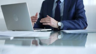 Mavi takım elbiseli bir işadamı, elleri cam ekrandaki dizüstü bilgisayarın yanında otururken parlak bir ofiste, internet iletişiminde, yakın çekim görüntüsünde oturuyor. İş konsepti.