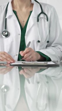 Kadın doktor, pano kullanıyor ve tıbbi bir ofisteki cam masaya notlar alıyor, dikey açıdan yakından bakıyor. Tıp konsepti.