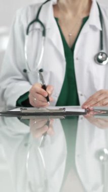 Kadın doktor, pano kullanıyor ve tıbbi bir ofisteki cam masaya notlar alıyor, dikey açıdan yakından bakıyor. Tıp konsepti.