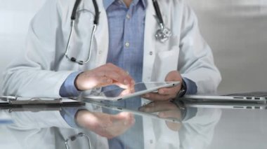 Tıbbi beyaz önlüğün altına mavi gömlek giyen doktor, modern sağlık ortamında dijital tablet kullanıyor, hasta verileriyle etkileşimde, yakın plan. Tıp konsepti.