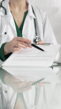 Hastane ortamındaki kadın doktor tıbbi raporlara işaret ediyor, yakın çekim çekimde uzmanlık gösteriyor. İlaç.