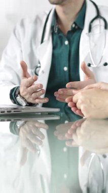 Steteskop ve laboratuvar önlüğü giyen doktor, masadaki bir hastaya dizüstü bilgisayarla teşhis koymayı açıklarken elleriyle işaret ediyor. Tıp konsepti.