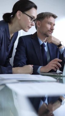 Modern bir ofis ortamında iş birliği yapan iki profesyonel, dizüstü bilgisayar kullanıyor ve bir projeyi tartışıyorlar, dikey portre. İş adamları konsepti.
