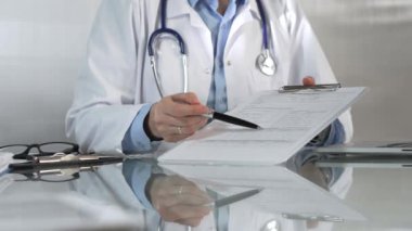 Hastane ortamındaki kadın doktor tıbbi raporlara işaret ediyor, yakın çekim çekimde uzmanlık gösteriyor. İlaç.