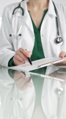 Hastane ortamındaki kadın doktor tıbbi raporlara işaret ediyor, yakın çekim çekimde uzmanlık gösteriyor. İlaç.