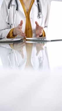 Stetoskop takan, laboratuvar önlüğünün altına sarı bluz giyen kimliği belirsiz doktor kadın klinikte dizüstü bilgisayarı olan cam bir masanın üzerinde el kol hareketi yapıyor. İlaç ve sağlık hizmetleri.