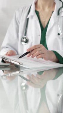 Hastane ortamındaki kadın doktor tıbbi raporlara işaret ediyor, yakın çekim çekimde uzmanlık gösteriyor. İlaç.