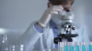 Laboratuvar tüpleri odaklandı, yakın görüş. Beyaz koruyucu eldivenli bilim adamı araştırmacı arka planda mikroskop kullanıyor. Tıp ve bilim konsepti.