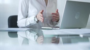 Beyaz bluzlu iş kadını elleri cam masadaki dizüstü bilgisayarın yanında otururken parlak bir ofiste, internet iletişiminde, yakın plan görüntüde oturuyor. İş konsepti.