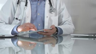 Tıbbi beyaz önlüğün altına mavi gömlek giyen doktor, modern sağlık ortamında dijital tablet kullanıyor, hasta verileriyle etkileşimde, yakın plan. Tıp konsepti.
