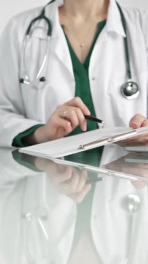 Hastane ortamındaki kadın doktor tıbbi raporlara işaret ediyor, yakın çekim çekimde uzmanlık gösteriyor. İlaç.