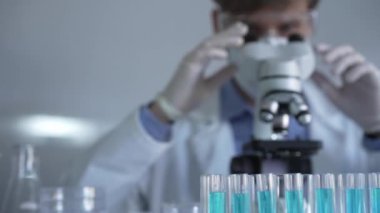 Laboratuvar tüpleri odaklandı, yakın görüş. Beyaz koruyucu eldivenli bilim adamı araştırmacı arka planda mikroskop kullanıyor. Tıp ve bilim konsepti.