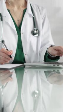 Kadın doktor, pano kullanıyor ve tıbbi bir ofisteki cam masaya notlar alıyor, dikey açıdan yakından bakıyor. Tıp konsepti.