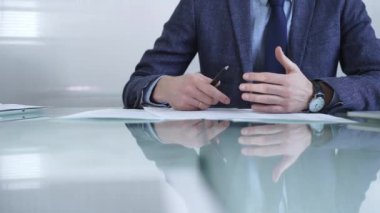 İş adamı sözleşme şartlarını inceliyor, modern ofis ortamında cam bir masada yansıması olan bir kalem kullanıyor. İş adamları veya denetim kavramı.