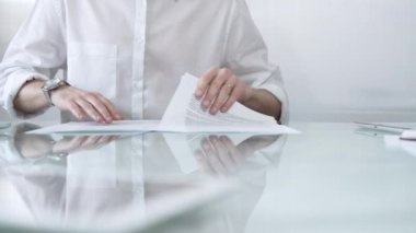 Beyaz gömlekli bir iş adamı, güncel ofis ortamında cam bir masada evrakları tutarken evrak işleriyle uğraşıyor. İş adamları konsepti.