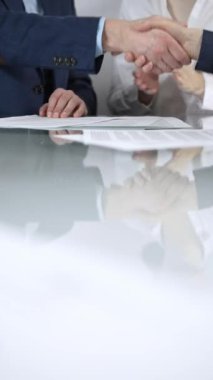 İş ortakları, ofis toplantısındaki cam masada sözleşme imzaladıktan sonra el sıkışıyor, anlaşma yapıyor ve el sıkışmayı dikey olarak kapatıyorlar..