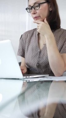 Kaslı noktalı bluzlu iş kadını dizüstü bilgisayar kullanıyor ve eli çenesinde düşünüyor. Parlak bir ofiste bir proje üzerinde çalışıyor. İş adamları konsepti.