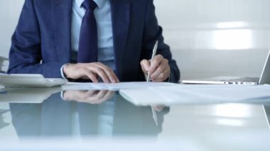 İş adamı hesap makinesi kullanıyor ve not alıyor. Ofis masasında dizüstü bilgisayar ve belgelerle çalışıyor. İş dünyasında denetim ve vergi teması.