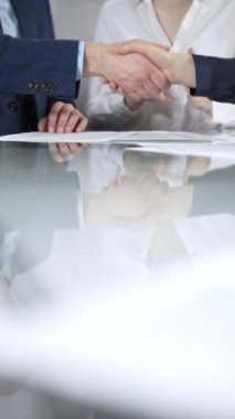 İş ortakları ofis toplantısındaki cam masada sözleşme imzaladıktan sonra el sıkışıyor, anlaşma yapıyor ve el sıkışmayı dikey olarak kapatıyorlar. Boşluğu kopyala.