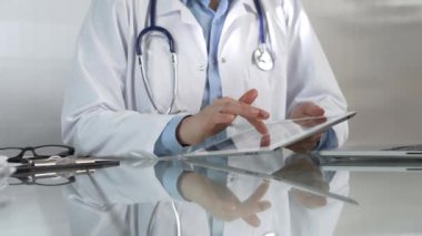 Doktor kadın, tıbbi önlüğün altına mavi bir bluz giyiyor, modern sağlık ortamında dijital tablet kullanıyor, hasta verileriyle etkileşimde, yakın plan. Tıp konsepti.