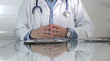 Mavi bluz, steteskop ve laboratuvar önlüğü giyen doktor kadın, cam bir masadaki hastaya dizüstü bilgisayarla teşhisi açıklarken elleriyle hareket ediyor. Tıp konsepti.