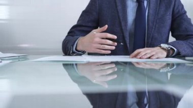 İş adamı sözleşme şartlarını inceliyor, modern ofis ortamında cam bir masada yansıması olan bir kalem kullanıyor. İş adamları veya denetim kavramı.