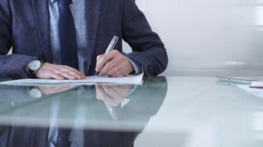 Çağdaş bir ofis ortamında modern cam bir masanın üzerinde profesyonel giyimli bir işadamı kalemle kontrat imzalıyor. İş adamları veya denetim kavramı