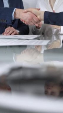 İş ortakları ofis toplantısındaki cam masada sözleşme imzaladıktan sonra el sıkışıyor, anlaşma yapıyor ve el sıkışmayı dikey olarak kapatıyorlar. Boşluğu kopyala.