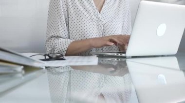 İş kadını dizüstü bilgisayarda klavye ile yazı yazıyor, vergiler ve denetim raporları hazırlıyor, belgeler ve cam masasında gözlüklerle. Vergiler, iş denetimleri.