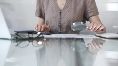 Kaslı bluz giyen iş kadını muhasebeci büyüteçle ve hesap makinesiyle mali raporları inceliyor, denetim yapıyor ve ofisindeki verileri analiz ediyor. Vergiler, iş denetimleri.