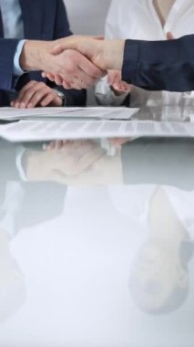 İş ortakları, ofis toplantısındaki cam masada sözleşme imzaladıktan sonra el sıkışıyor, anlaşma yapıyor ve el sıkışmayı dikey olarak kapatıyorlar..