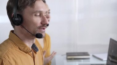 Sarı günlük gömlekli odaklı erkek çağrı merkezi operatörü müşterilerine çevrimiçi olarak yardım ediyor, müşteri desteği sağlıyor ve sorulara cevap veriyor. Çağrı merkezi operatörleri.