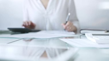 Finansal belgelerin klasörleri cam masanın üzerinde duruyor ve hesap makinesiyle kadın muhasebecinin yanında işlem için bekliyor ve ofiste notlar alıyor. Vergiler, iş konsepti denetimi.
