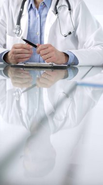 Stetoskop, mavi gömlek ve laboratuvar önlüğü giyen kimliği belirsiz erkek doktor klinikte dizüstü bilgisayarlı cam bir masa ve dikey yakın görüş ile el kol hareketi yapıyor. Tıp konsepti.