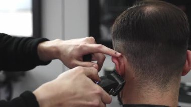Profesyonel berber, modaya uygun bir berber dükkanında bir adamın saçını elektrikli makasla ustaca kesiyor, müşterileri daha şık ve modern bir saç stili yaratıyor.