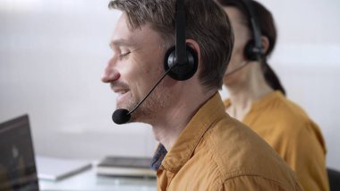 Sarı günlük gömlekli odaklı erkek çağrı merkezi operatörü müşterilerine çevrimiçi olarak yardım ediyor, müşteri desteği sağlıyor ve sorulara cevap veriyor. Çağrı merkezi operatörleri.