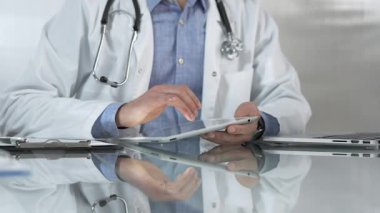 Tıbbi beyaz önlüğün altına mavi gömlek giyen doktor, modern sağlık ortamında dijital tablet kullanıyor, hasta verileriyle etkileşimde, yakın plan. Tıp konsepti.