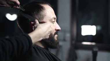 Profesyonel berber erkek müşterinin sakalını elektrikli budayıcı kullanarak dikkatlice şekillendiriyor, modern berber dükkanında titiz bir bakım ve stil sağlıyor.